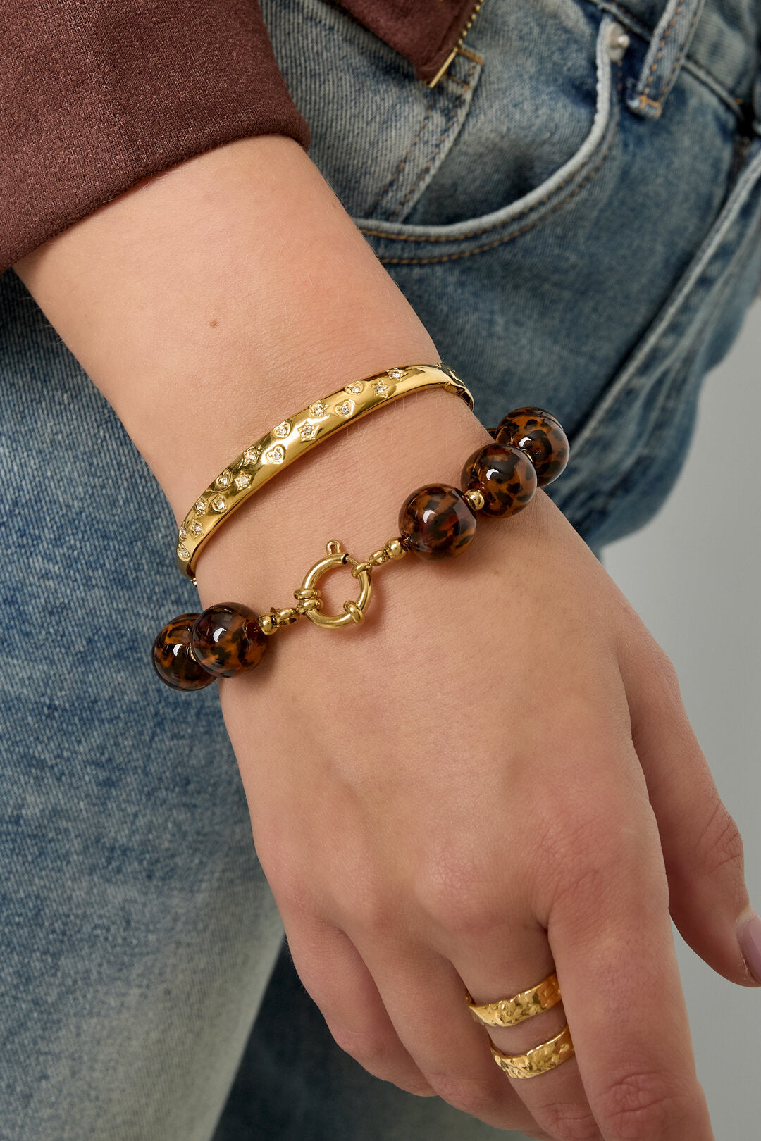 Armbandenset met twee stukken: goudkleurige bangle met diamanten hartjes en bruine tortoiseshell kralenarmband op de pols.