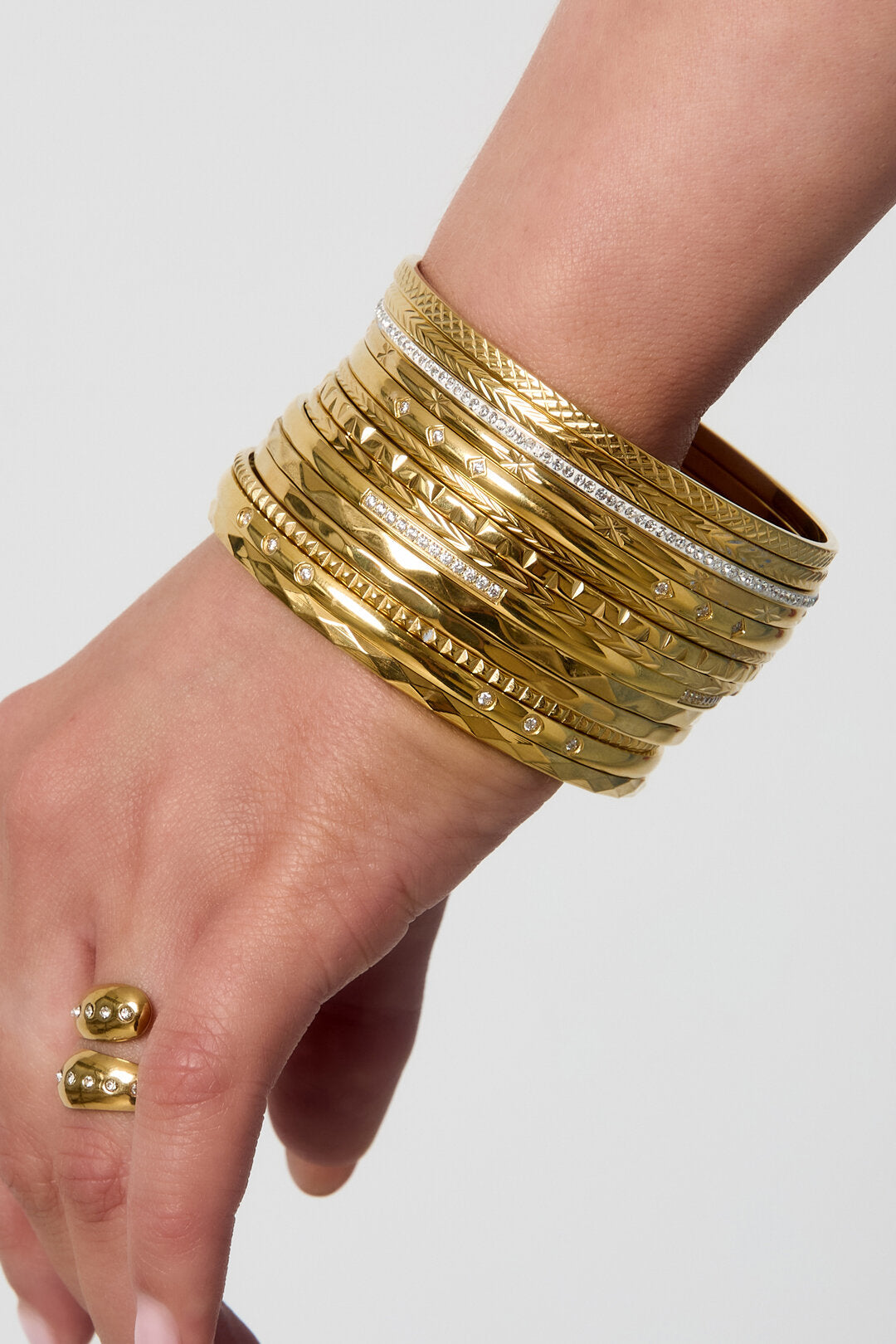 Gladde bangle stack in gold-tone on wrist, featuring varied textured bands and crystal accents across about 12 bangles.